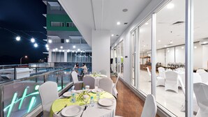 Un ristorante con tavoli rotondi, sedie bianche e vista su un edificio dall'altra parte dell'acqua.