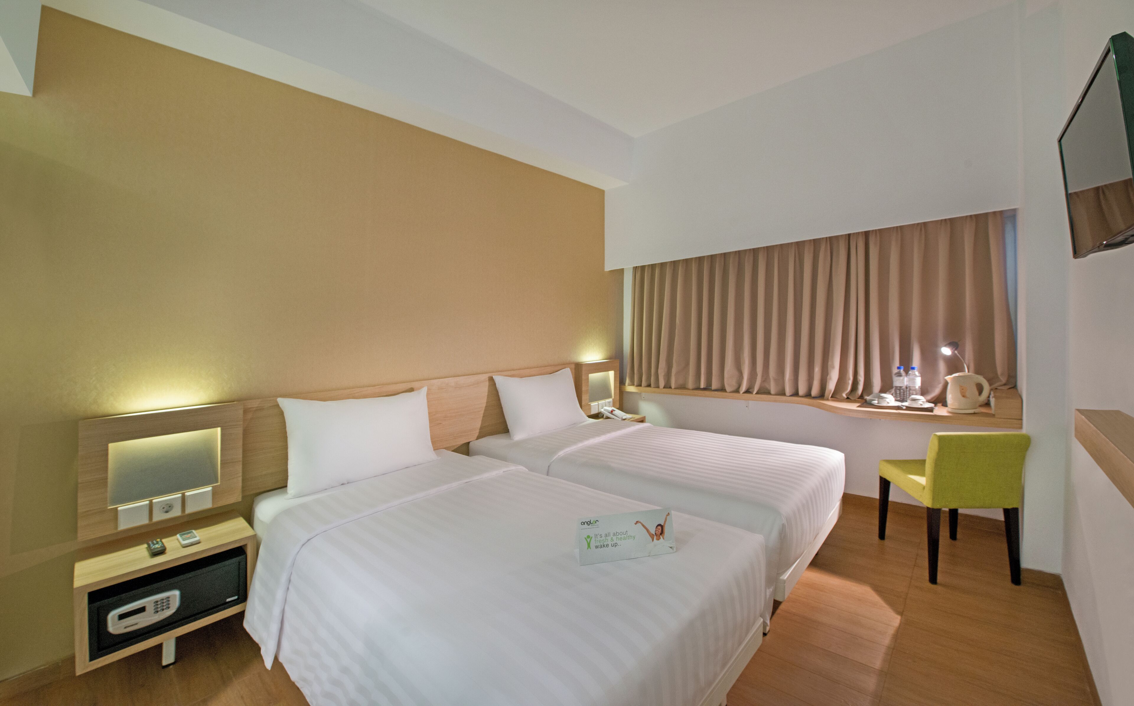 A hotel room with two beds, a desk with a chair, a TV, and a window with curtains.
