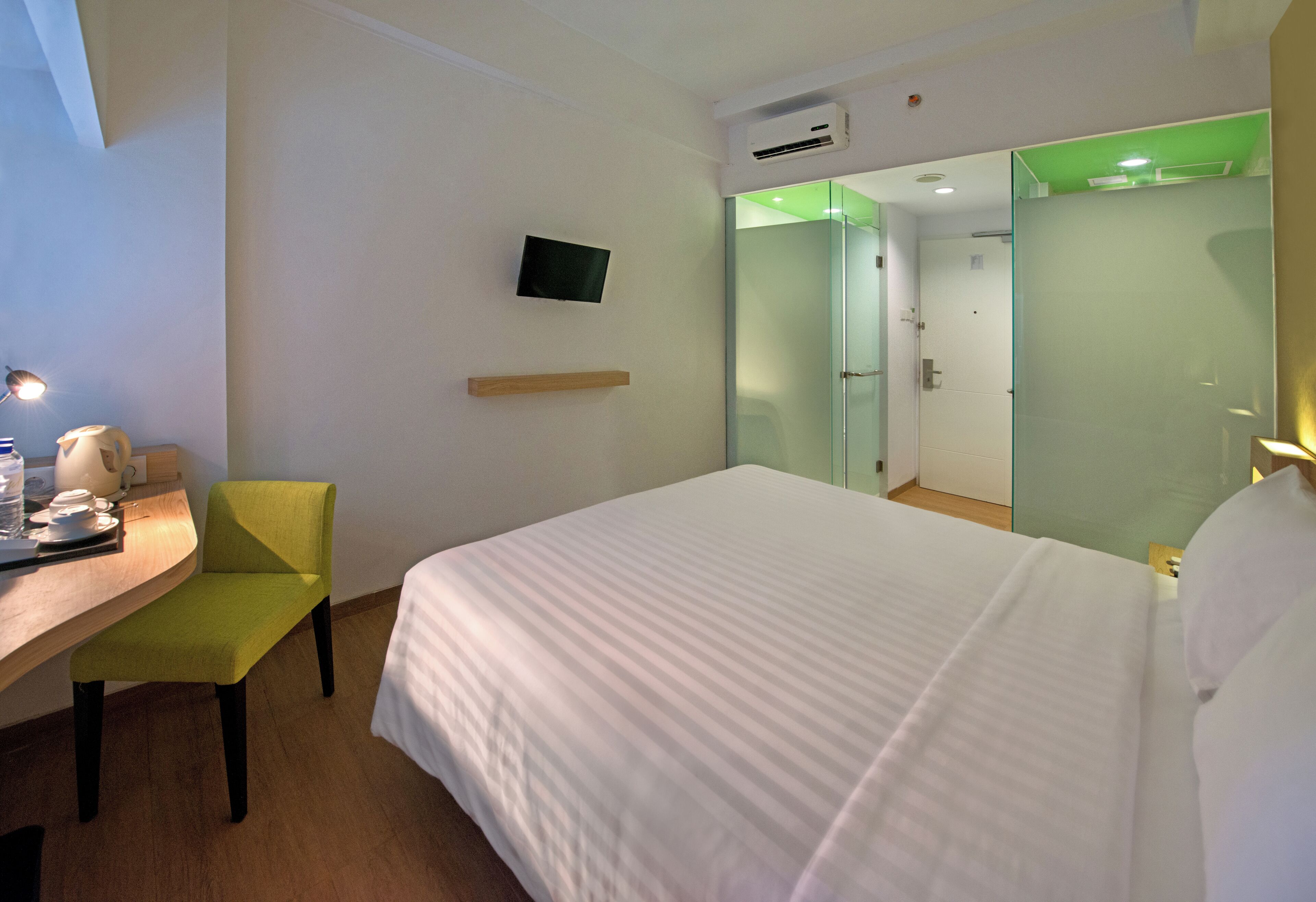 A hotel room with a bed, a desk with a chair, a television, and a mirror.