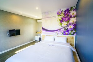 A modern hotel room with a large bed, a flat-screen TV mounted on the wall, and a decorative floral mural. - Monteview Stay (Seogwipo)