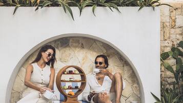 Two people sitting at a table with a dessert display between them, in an outdoor setting with plants and a stone wall.