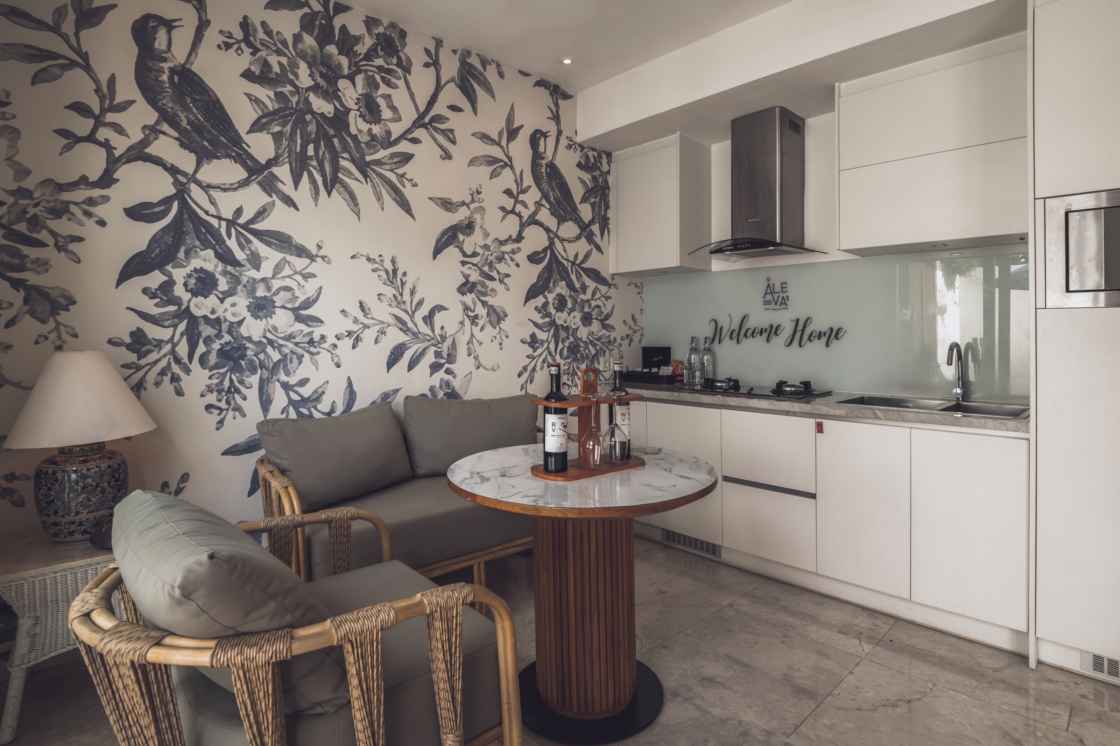 Une cuisine moderne avec un coin repas, comprenant une table ronde, des chaises en osier, un canapé et un papier peint à motifs floraux.
