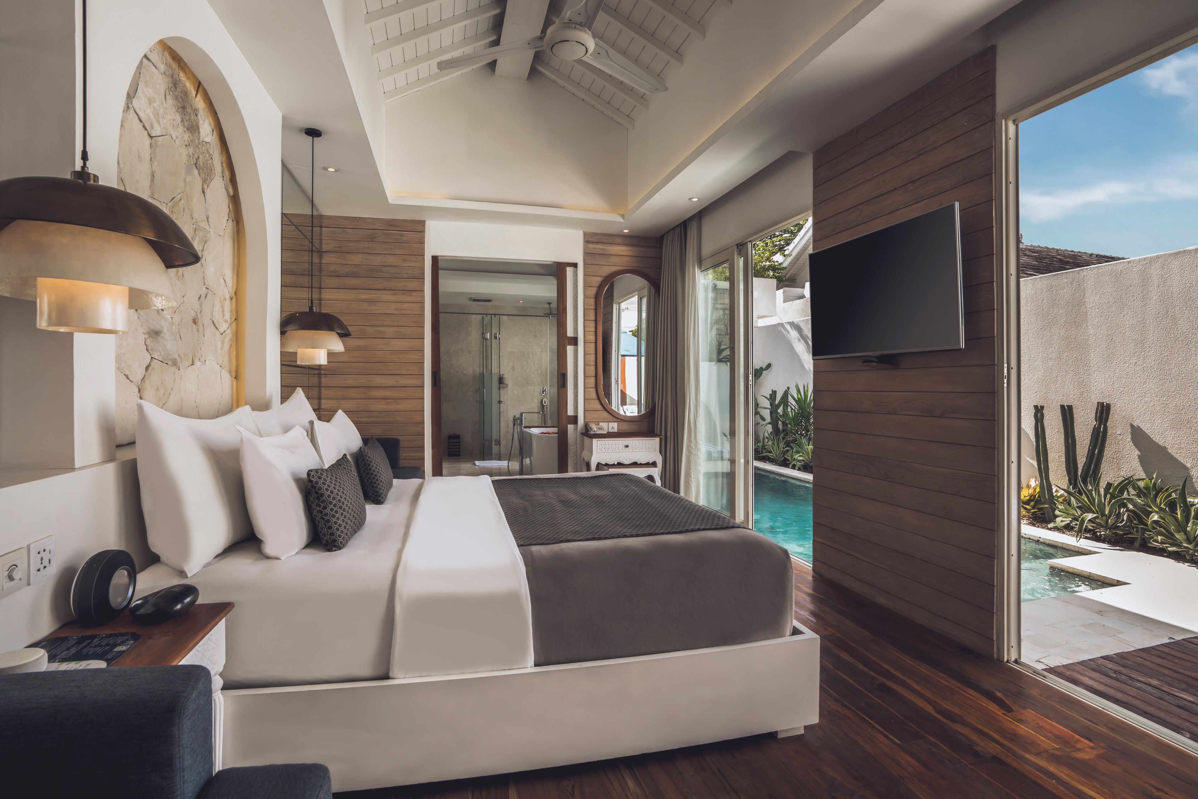 Ein modernes Schlafzimmer mit einem großen Bett, einem Fernseher und Blick auf einen Swimmingpool.