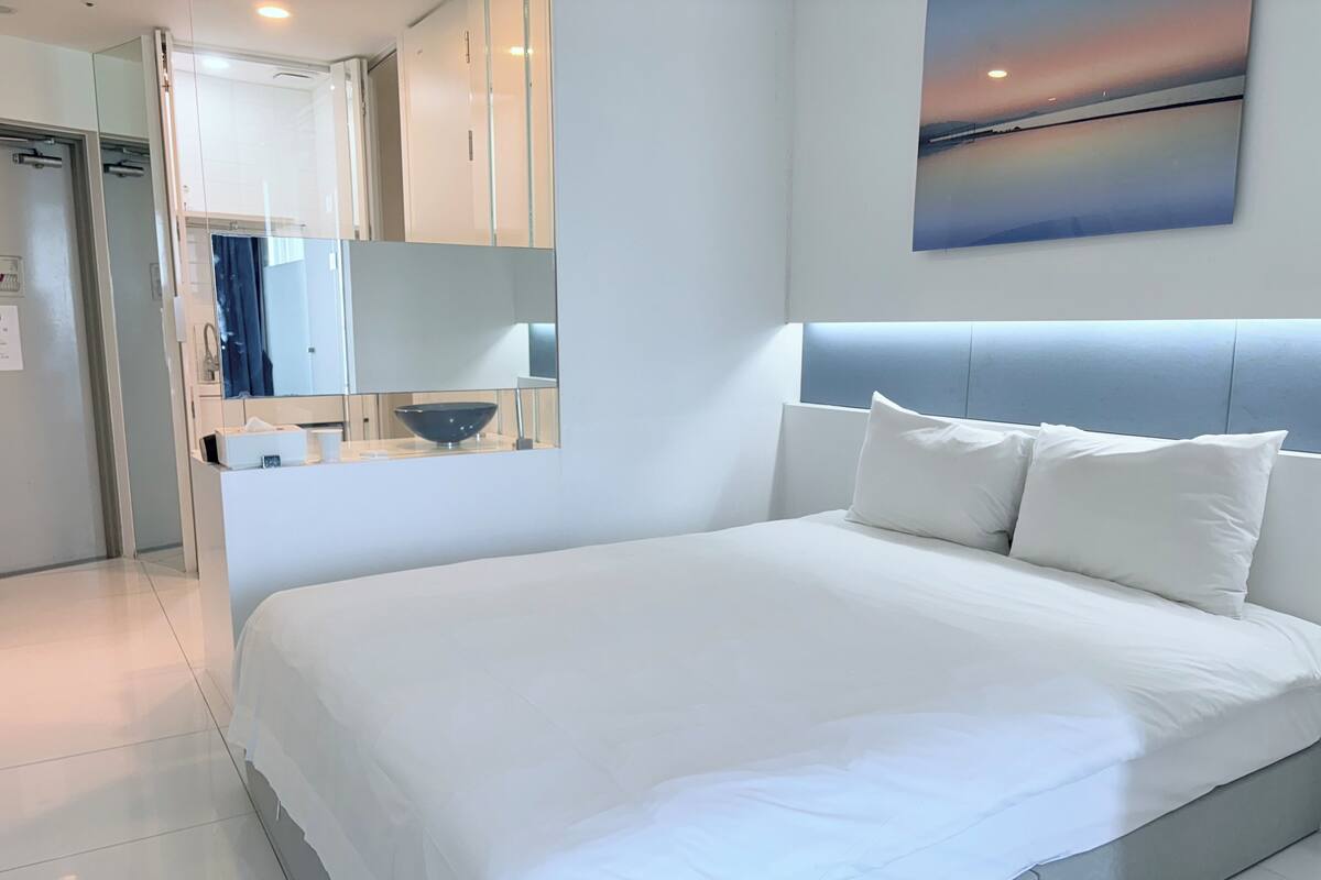 A modern hotel room with a large bed, a nightstand, a mirror, and a painting on the wall.