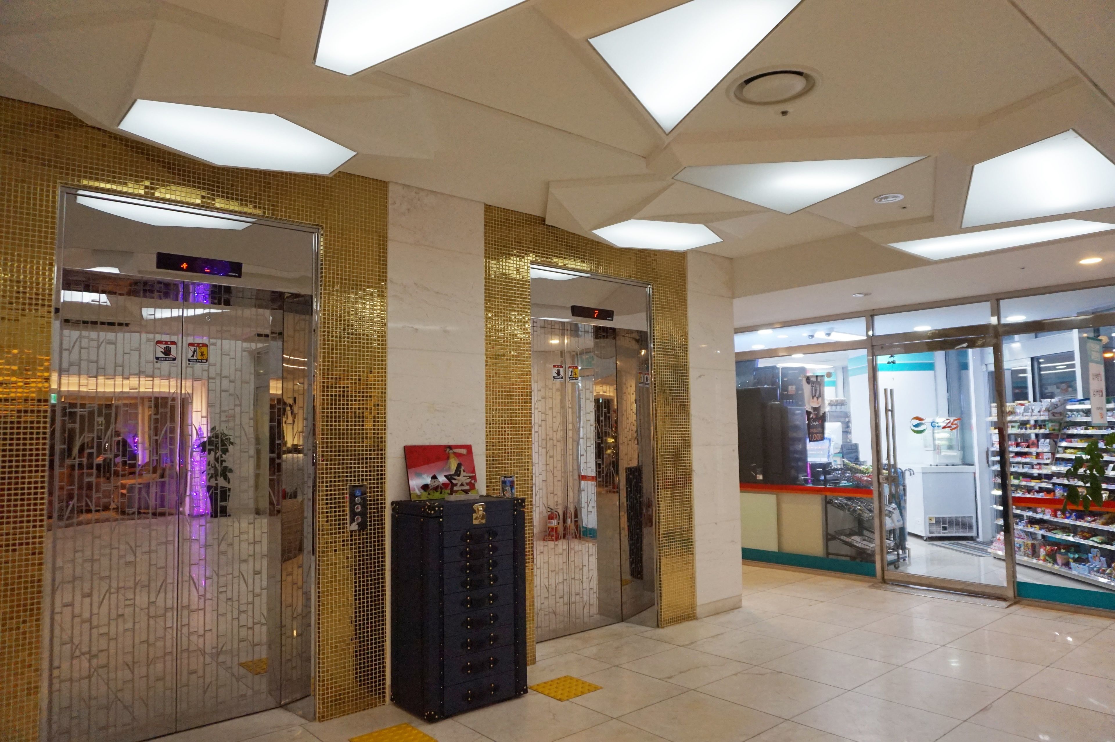Un vestíbulo de hotel con dos ascensores, una máquina expendedora y la entrada visible a una tienda.