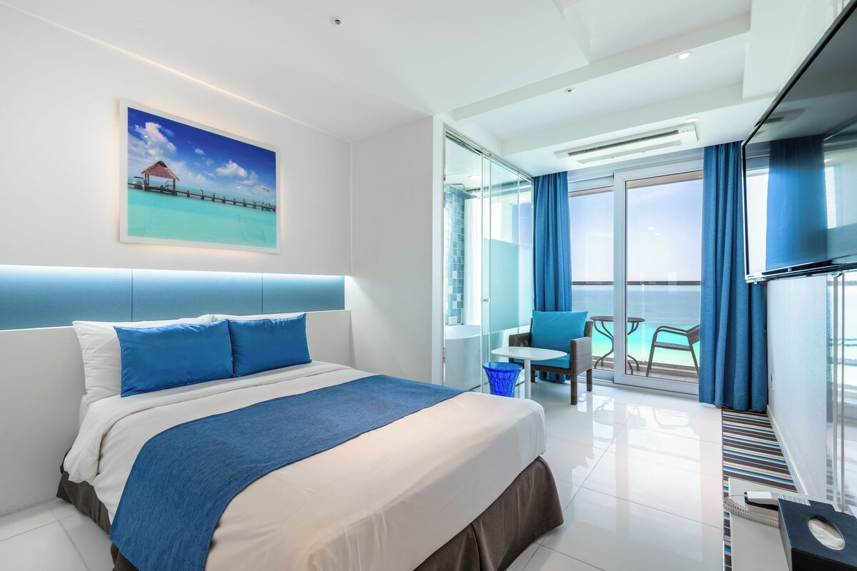 Una habitación de hotel moderna con una cama grande, un balcón con vistas y un área de comedor.