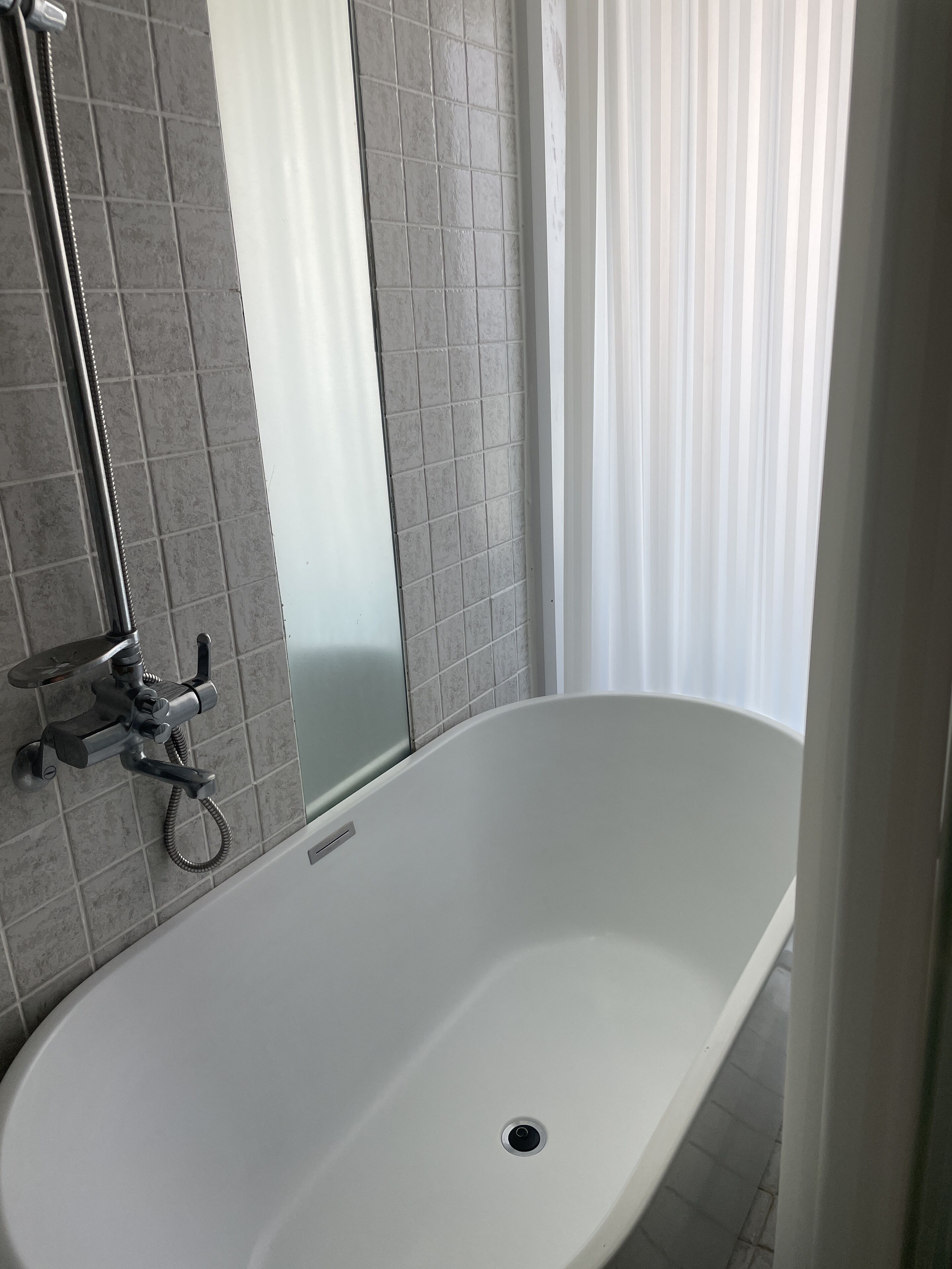 A modern bathroom with a freestanding bathtub, a showerhead, and a mirror.