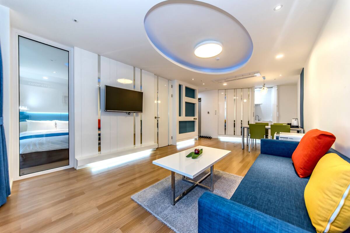 A modern hotel room with a bed, a dining area, and a TV.