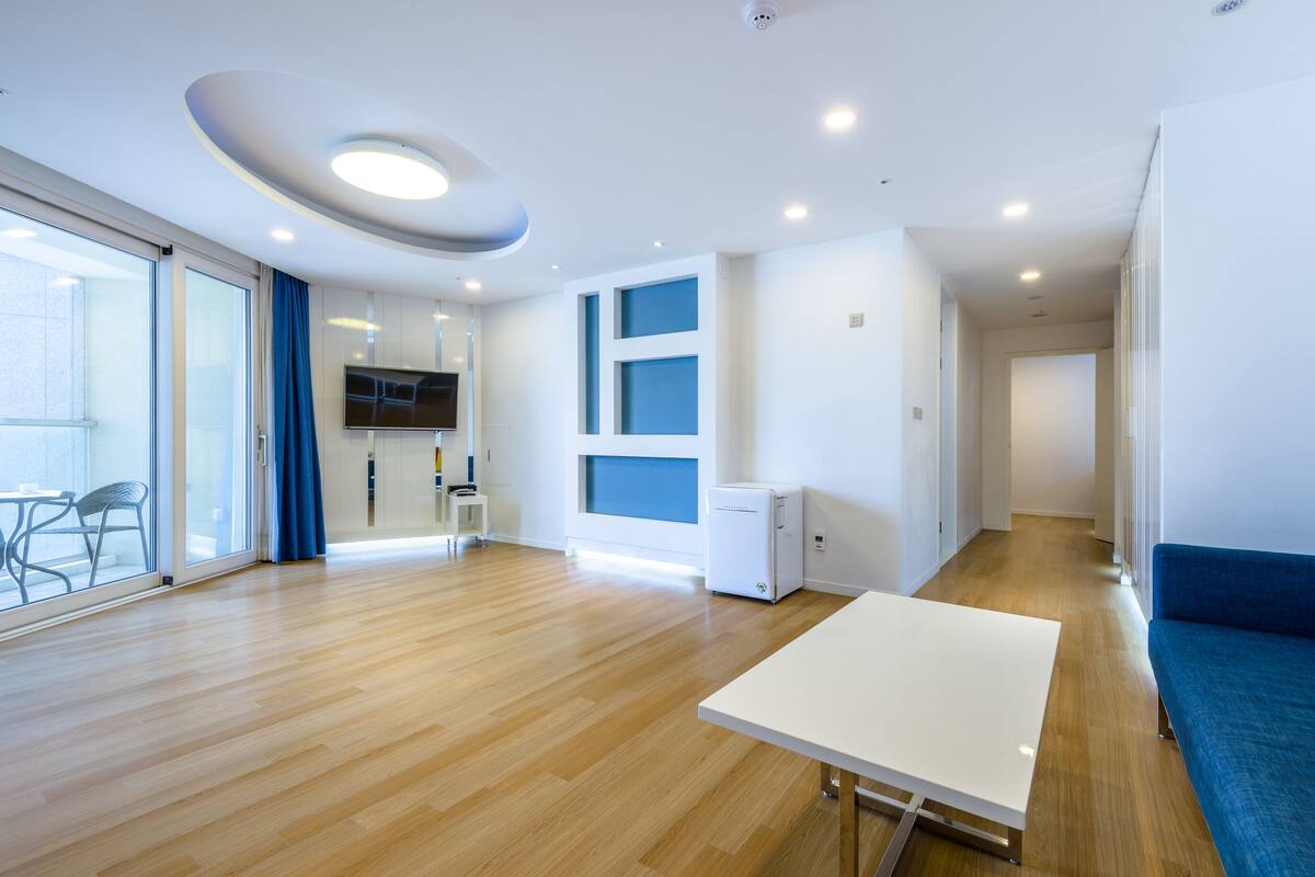 A modern living room with a wooden floor, a white table, a blue sofa, and a flat-screen TV.