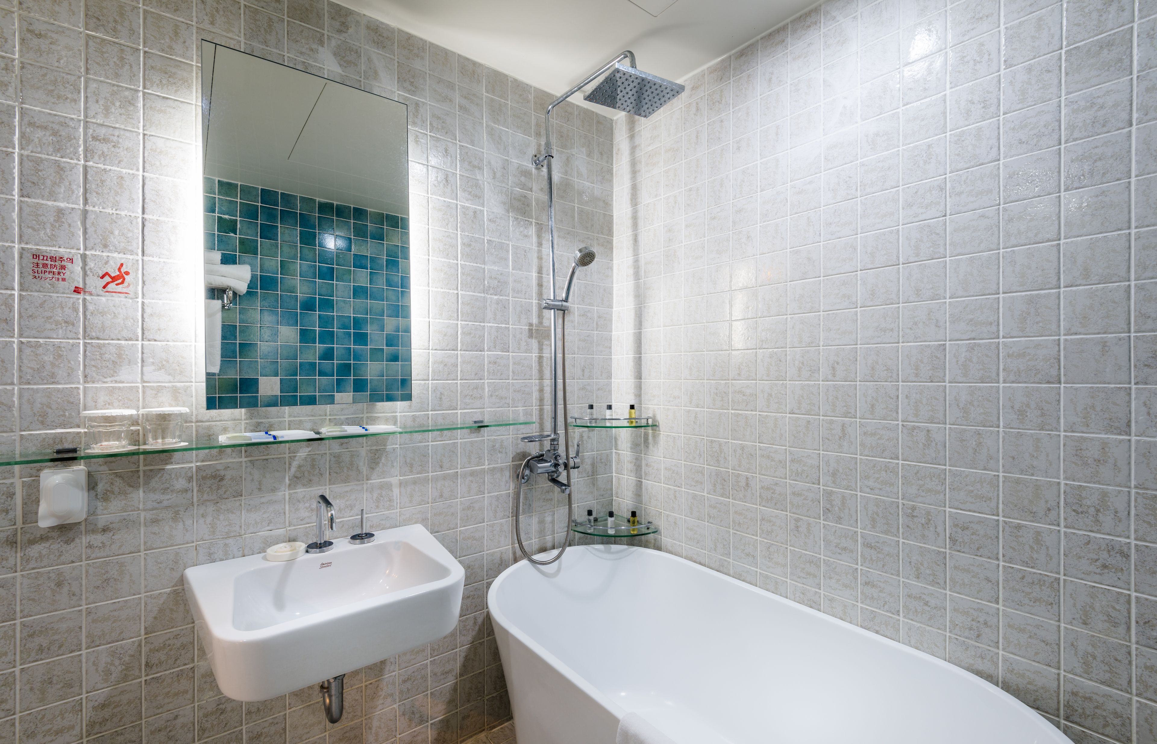 Een badkamer met een wit wastafel, een glazen plank, een spiegel en een douche.