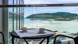 A balcony with a table and chairs overlooking a beach and a hilly landscape.