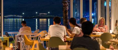 A restaurant with outdoor seating overlooking a body of water at night.