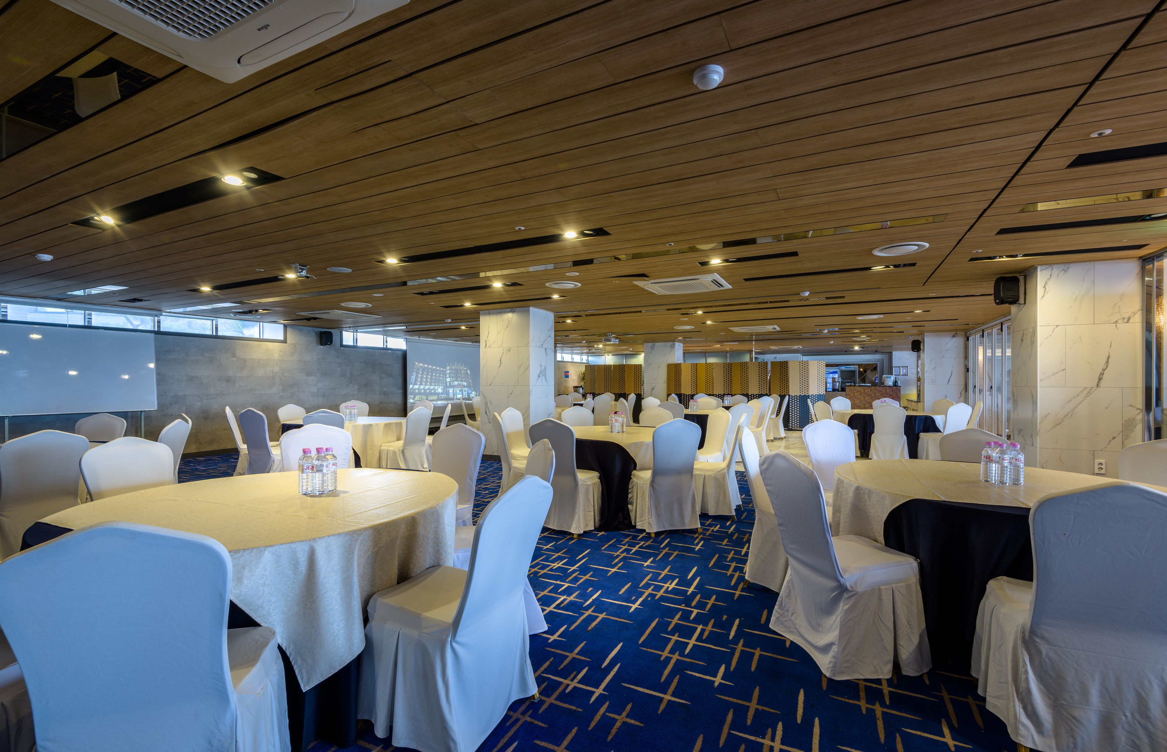 Un salón de conferencias con mesas redondas, sillas blancas y alfombra azul.