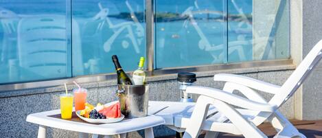 A balcony with a table set for two, featuring a bottle of champagne, a glass of orange juice, and a plate with watermelon and blueberries.