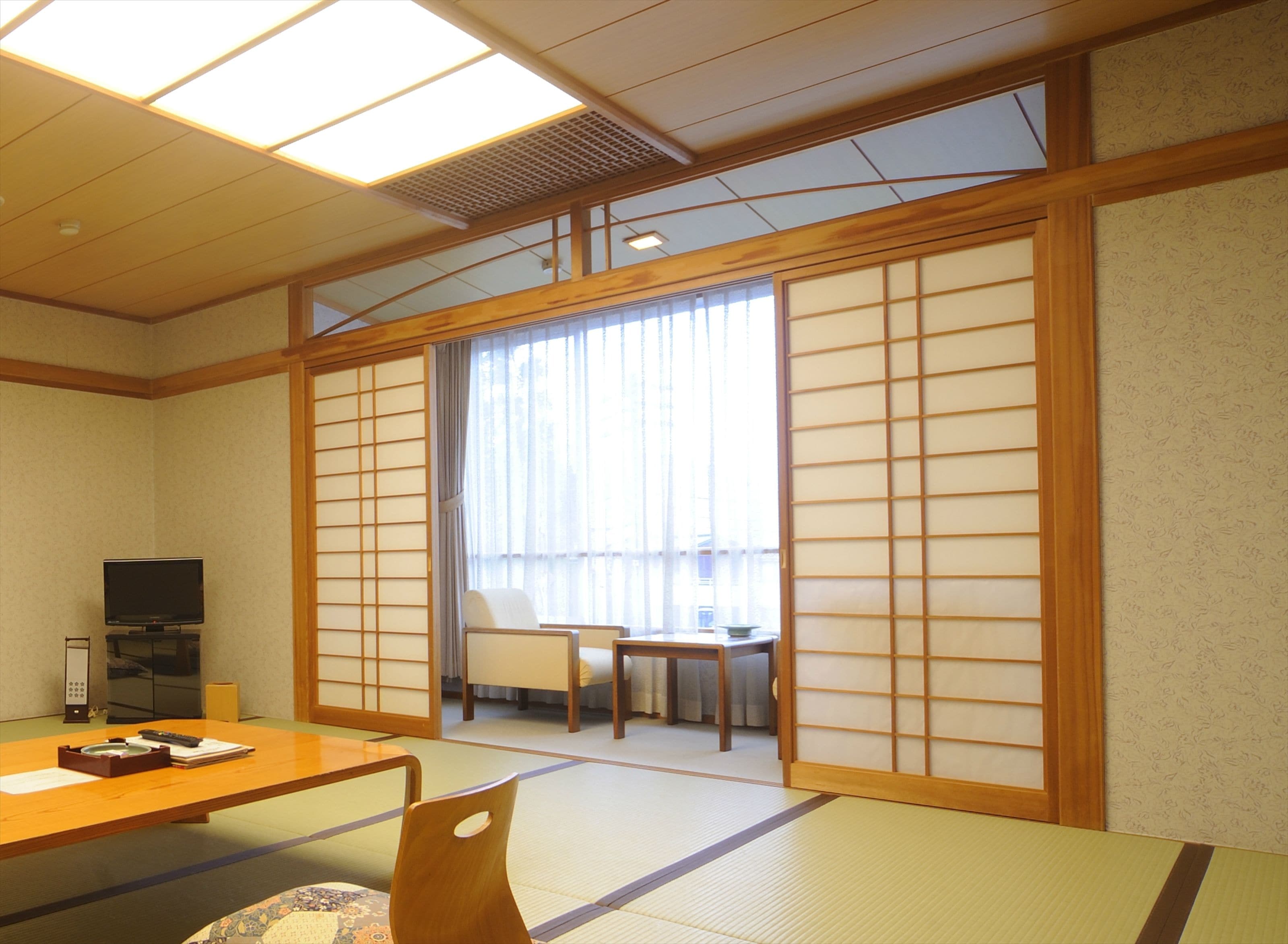 A traditional Japanese room with tatami flooring, a low table, a television, and sliding doors.