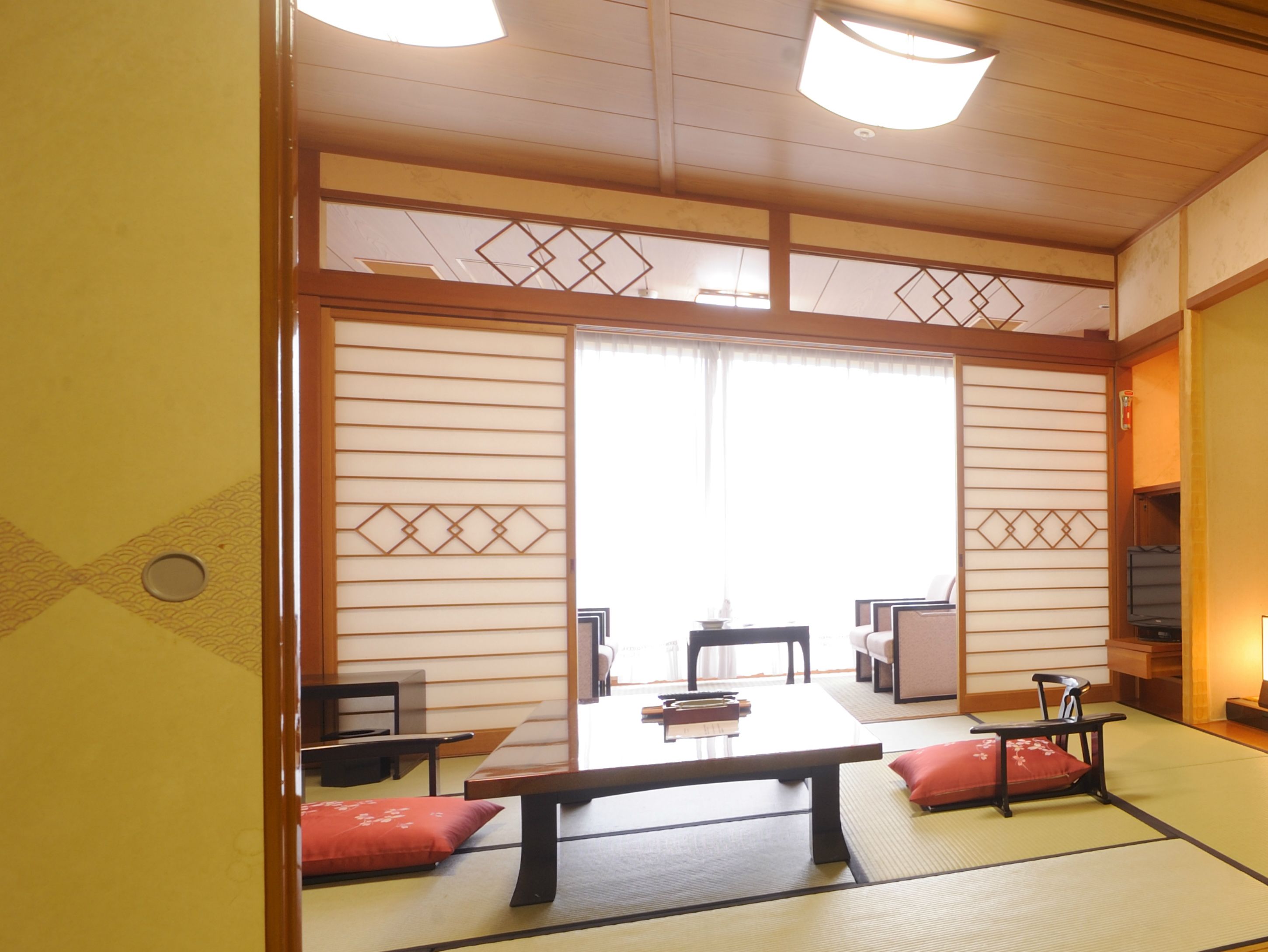 A traditional Japanese room with tatami flooring, a low table, two chairs, and a sliding door with decorative patterns.