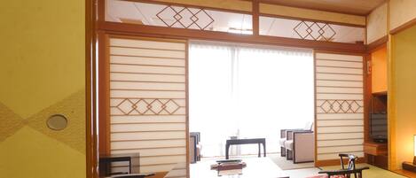 Una habitación japonesa tradicional con suelo de tatami, una mesa baja, dos sillas y un puertas correderas con motivos decorativos.