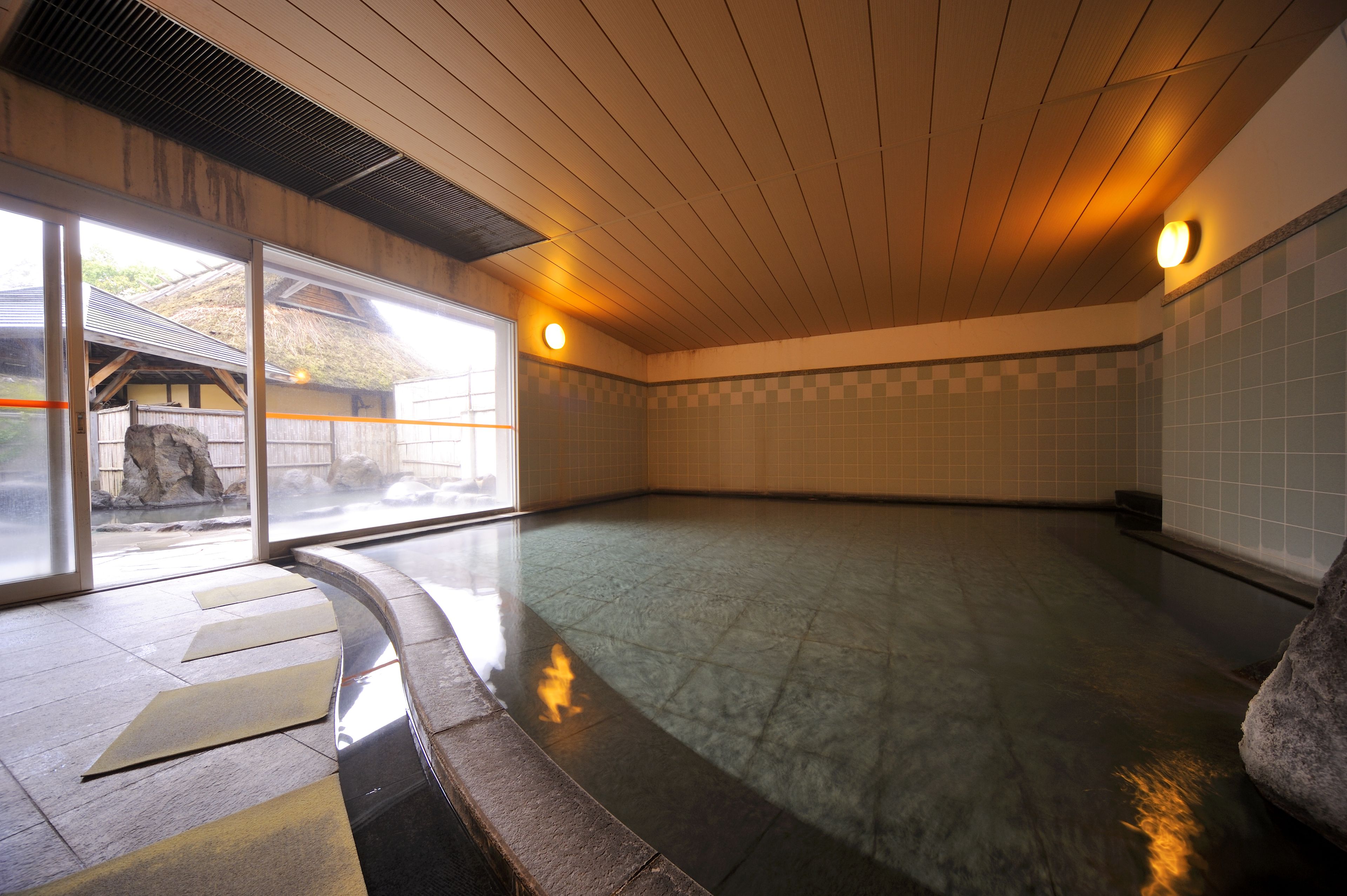 A spacious indoor area with a tiled floor, wooden ceiling, and large windows.
