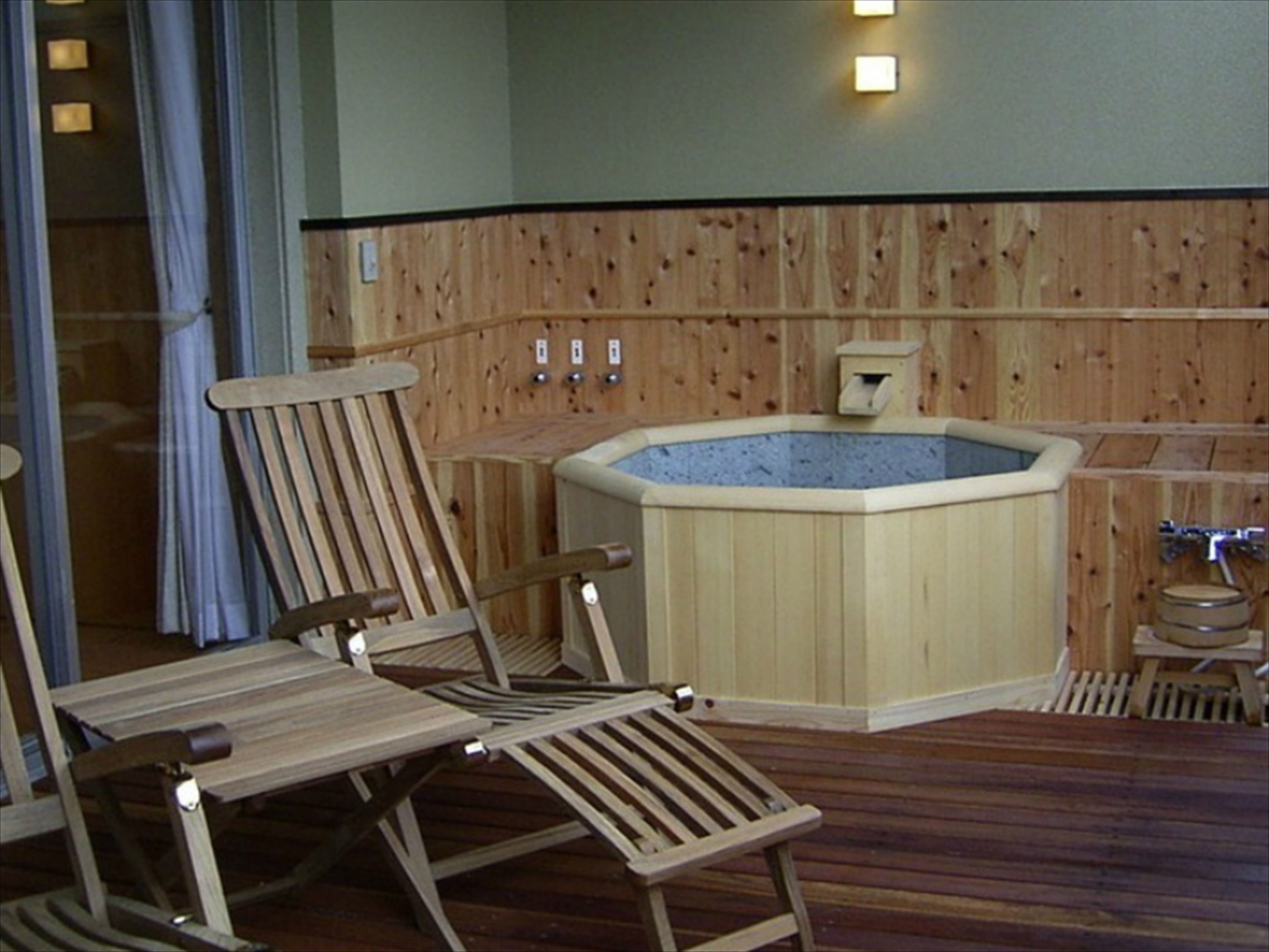 Une terrasse en bois avec un jacuzzi, des chaises en bois et un mur en bois agrémenté d’un luminaire.