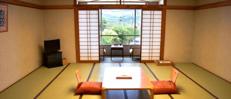 A tatami room with a low table, two chairs, a television, and a view through shoji screens.