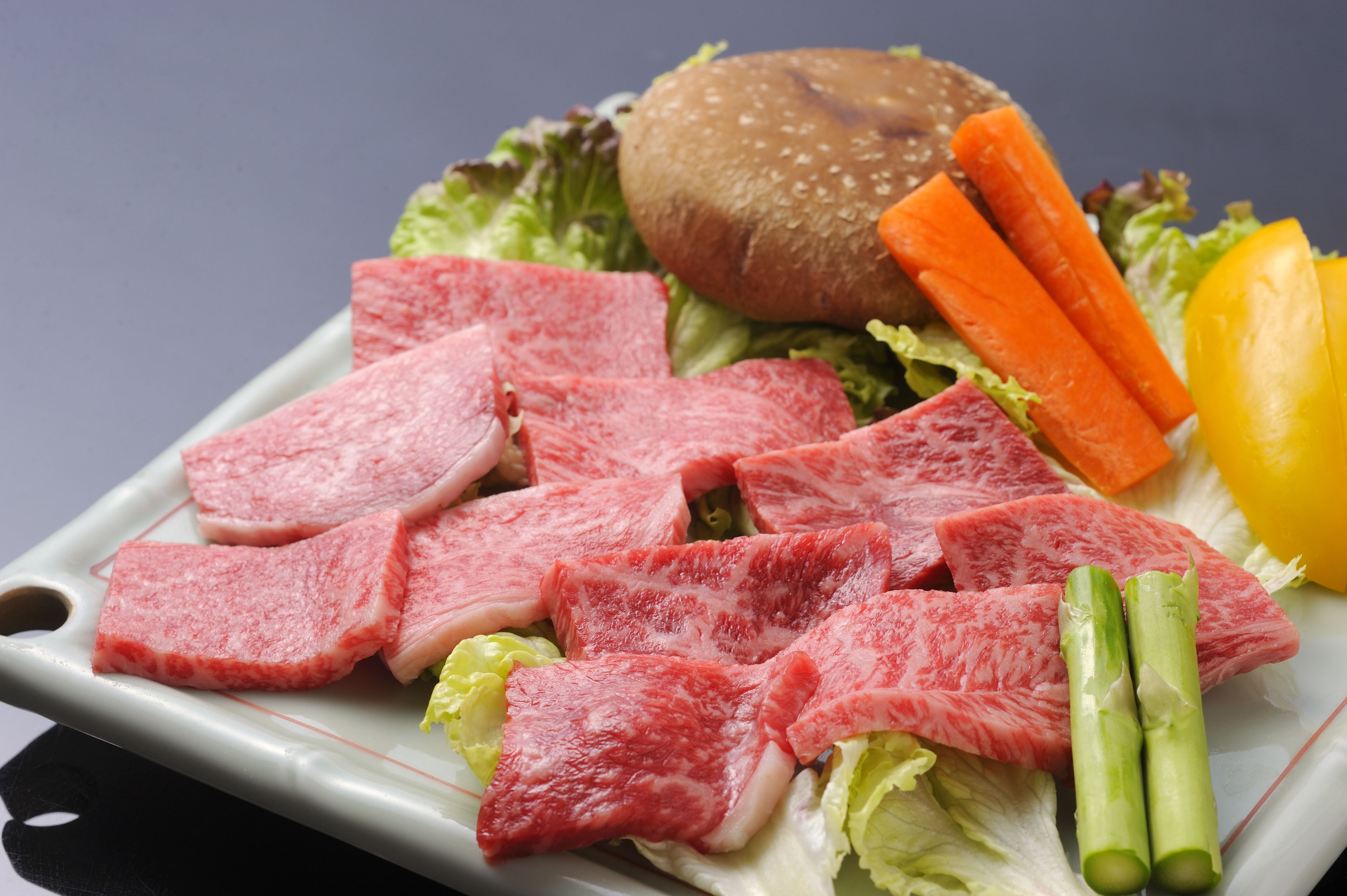 A plate with sliced meat, vegetables, and a burger.