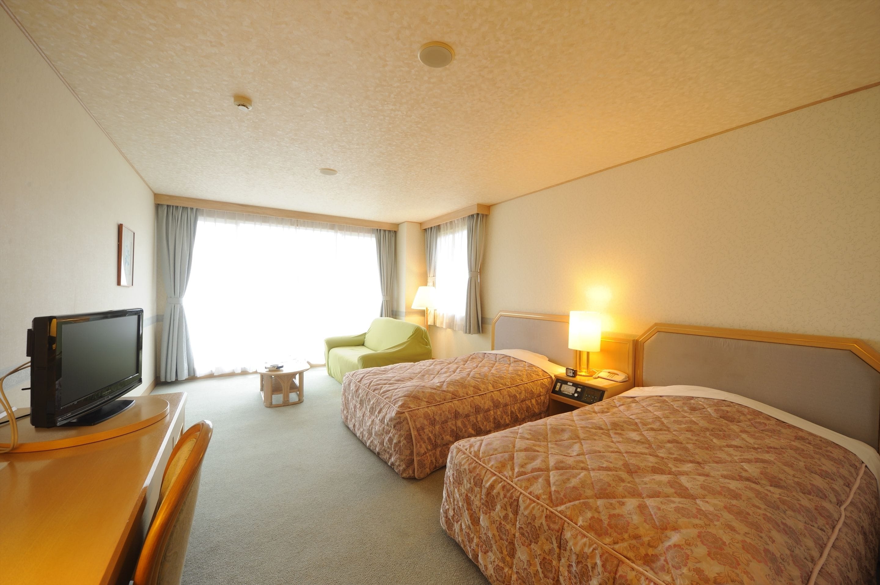 A hotel room with two beds, a desk with a television, a chair, and a lamp.