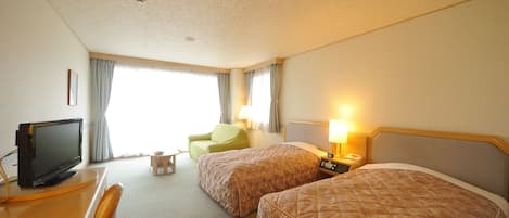 A hotel room with two beds, a desk with a television, a chair, and a lamp.