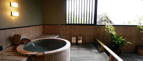 A wooden hot tub with a wooden bench and a potted plant.