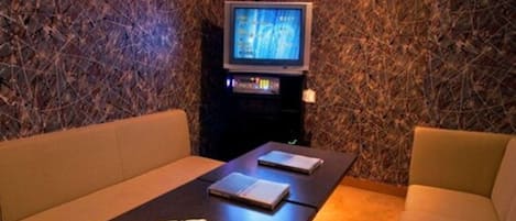 A room with a TV on a stand, two sofas, and a small table with a device on it.