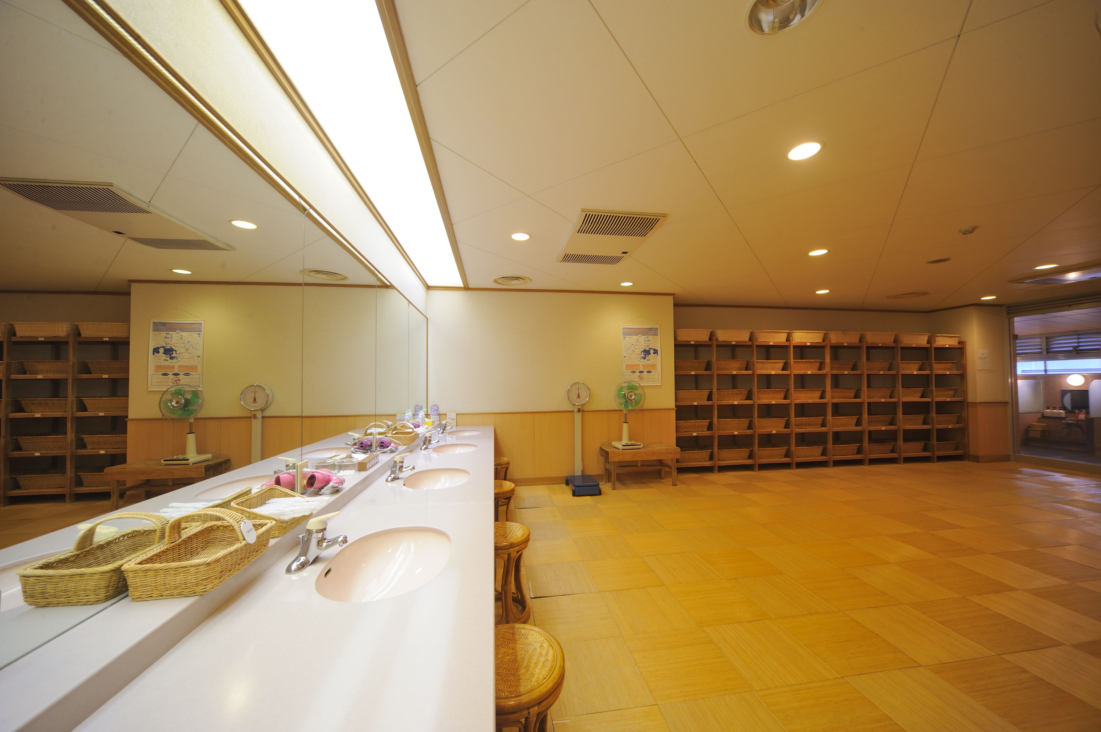 A clean, well-lit bathroom with multiple sinks, wicker baskets, and wooden shelves.