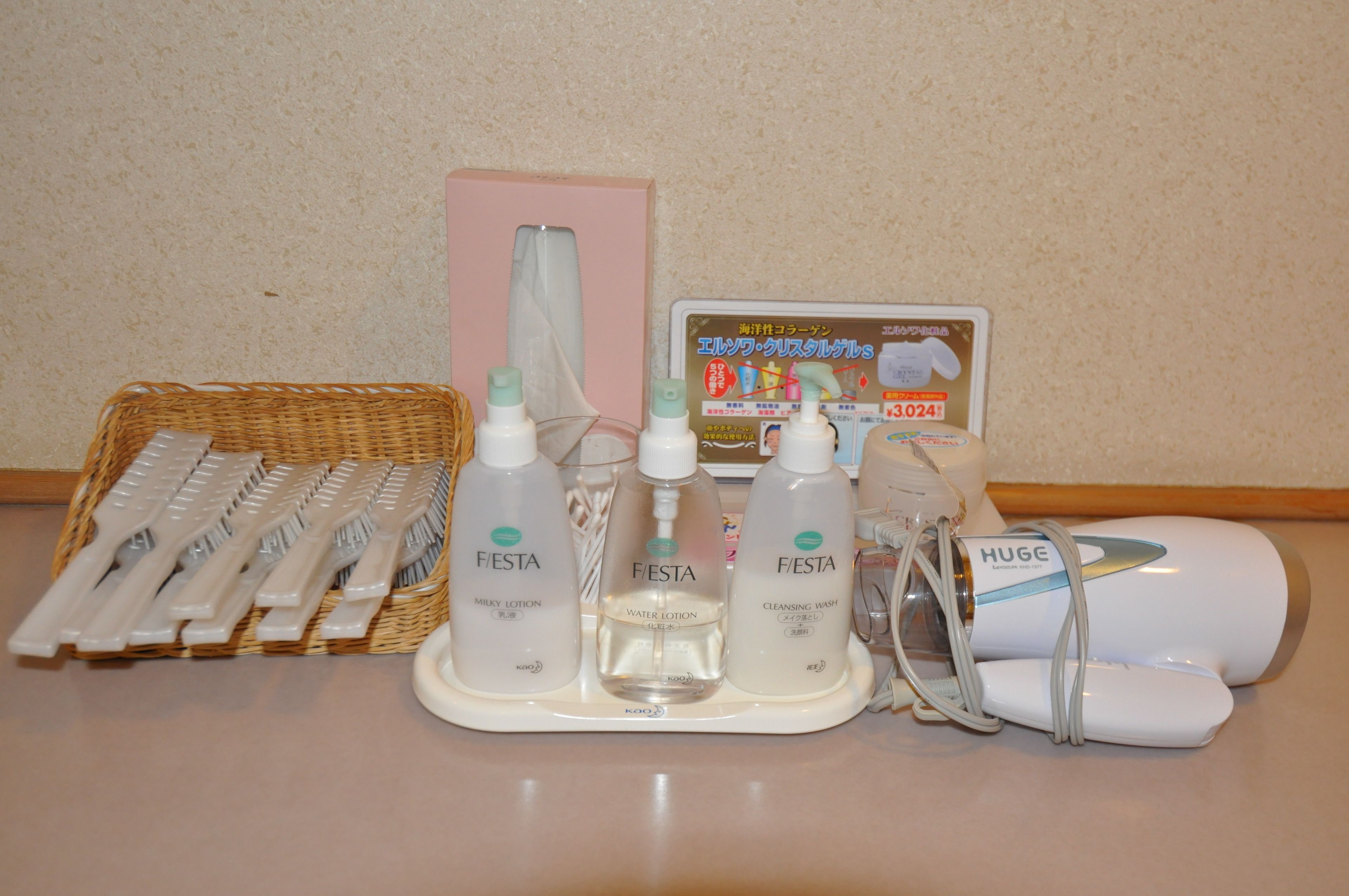 A bathroom vanity with a basket of toothbrushes, three bottles of FIESTA products, a facial cleansing brush, and a hairdryer.