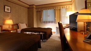 Una habitación de hotel con dos camas, un escritorio con computadora, teléfono y televisor.