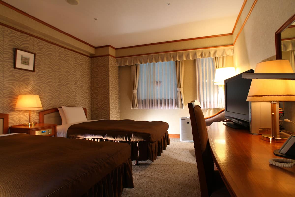 A hotel room with two beds, a desk with a computer, a telephone, and a television.