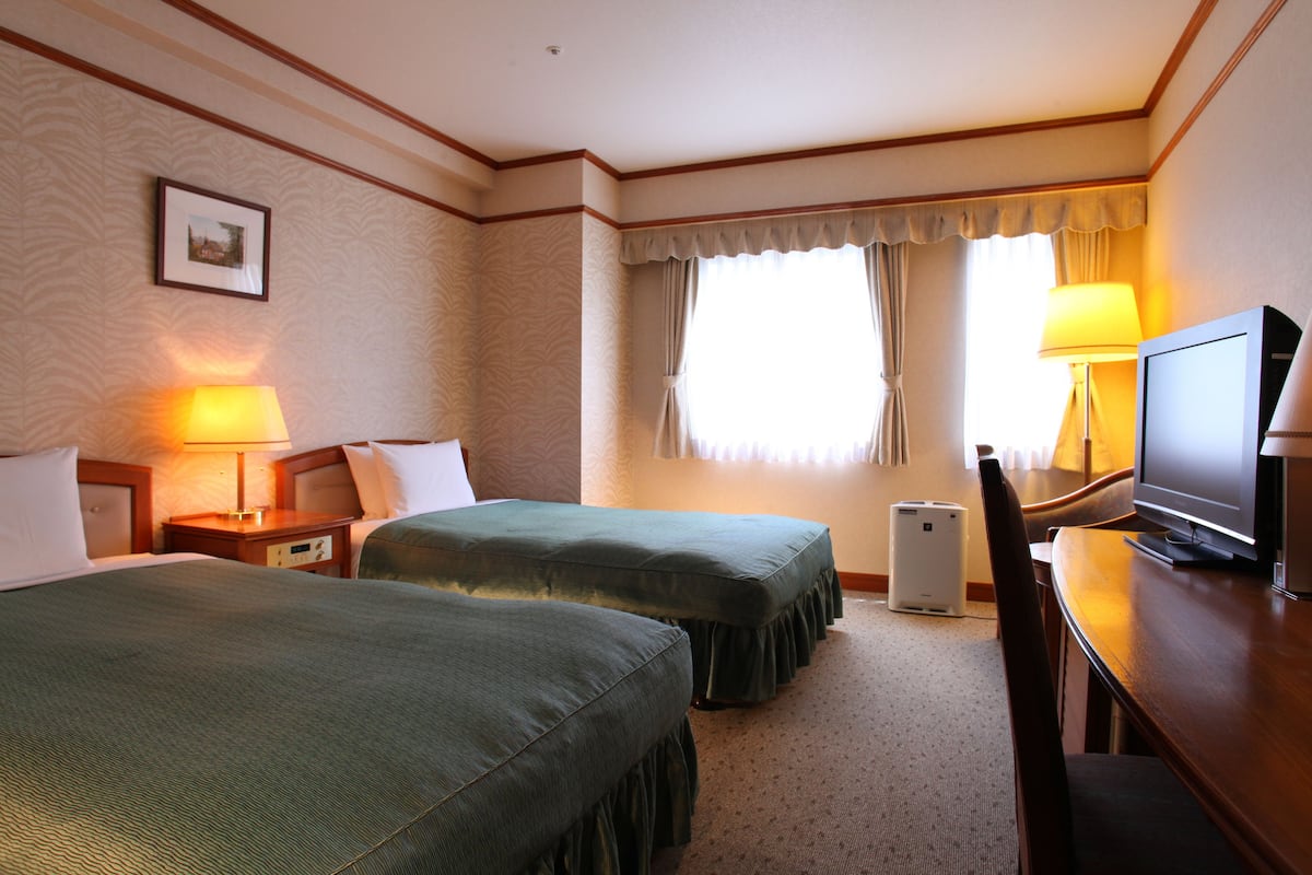 A hotel room with two beds, a television, a desk, and a lamp.