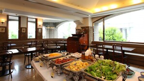Montaje de bufé con diversas opciones de comida y disposición de mesas en un comedor con amplias ventanas.