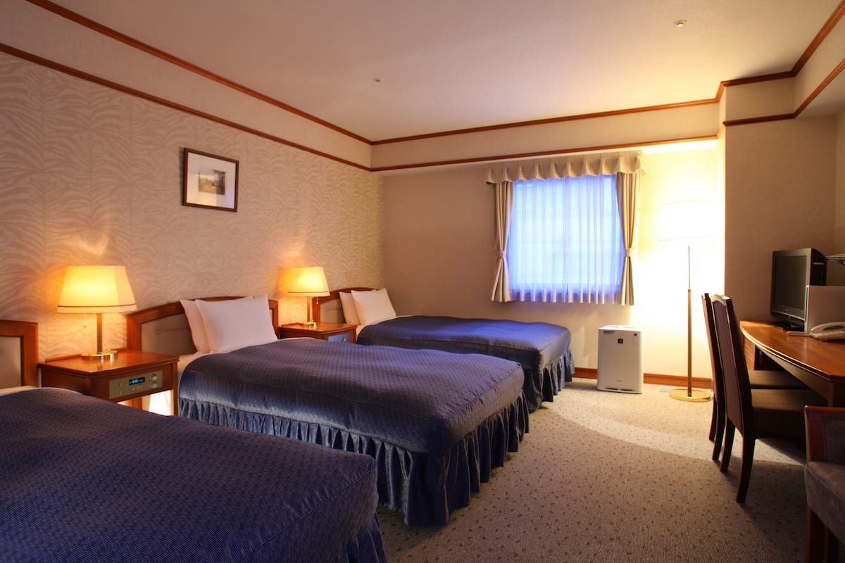 A hotel room with two beds, a desk, a chair, a television, and a window with curtains.