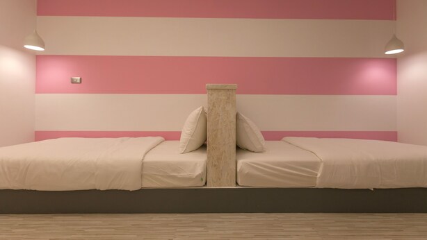 Una habitación con dos camas, una pared a rayas rosa y blanca, y un pilar de mármol.