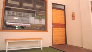 Una habitación con puerta de madera, un banco y ventana con vista a un edificio.