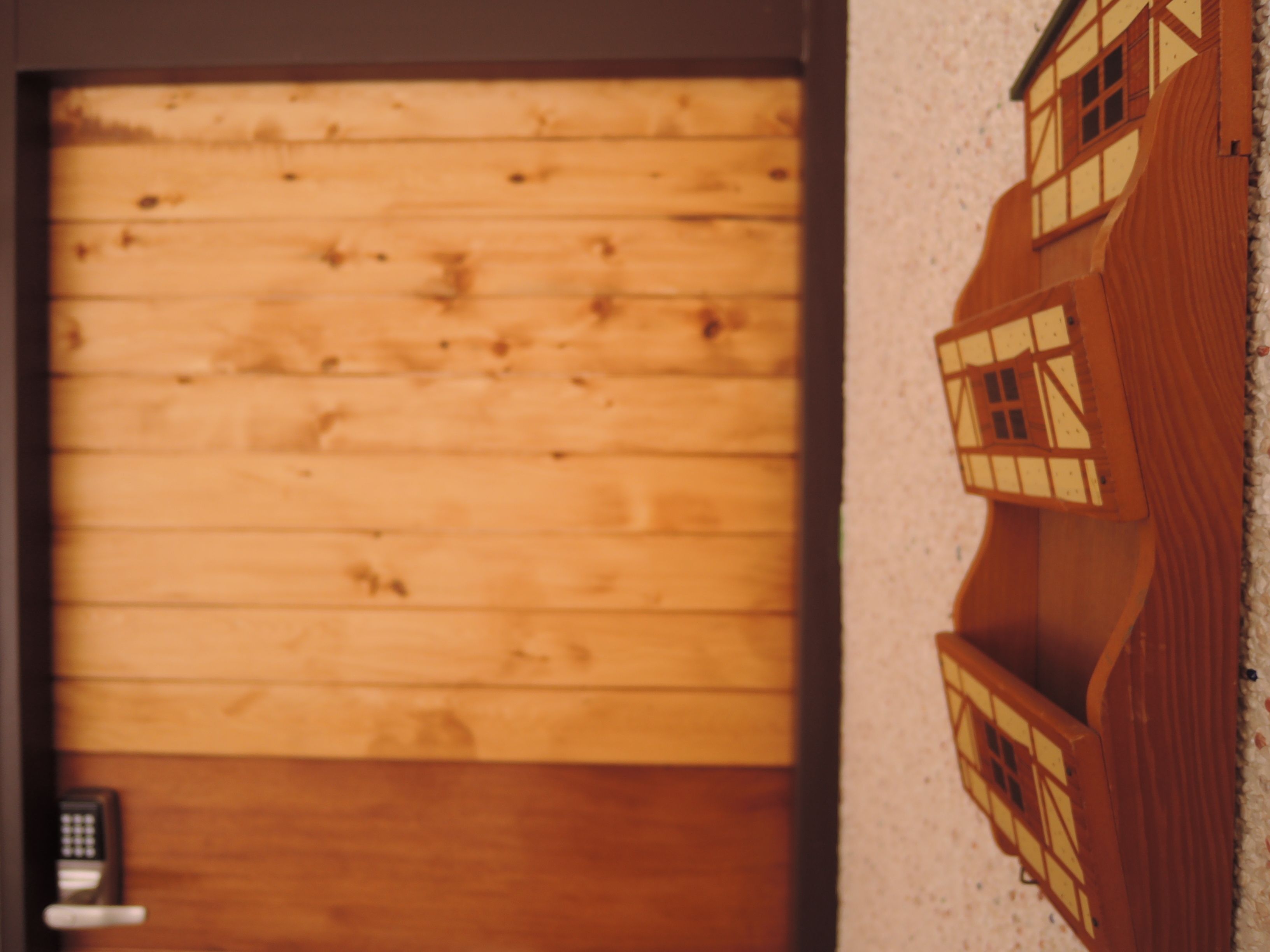 A wooden door with a keypad lock and a small model house on the wall.