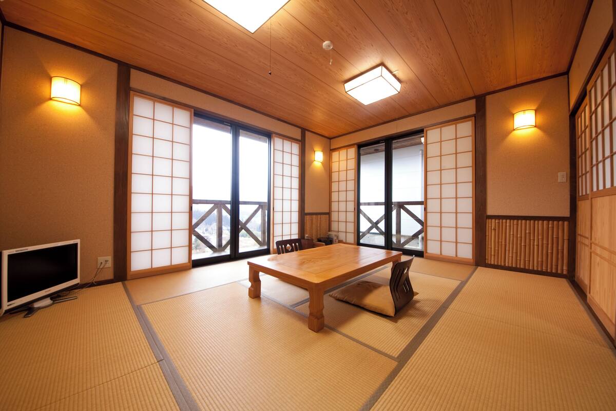 Een traditionele Japanse kamer met tatami vloerbedekking, een houten tafel, schuifdeuren en een televisietoestel.