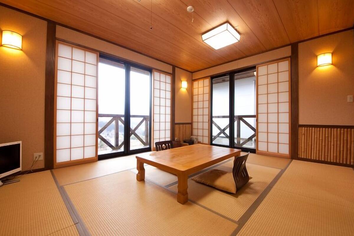 Une pièce de style japonais traditionnel, avec un sol recouvert de tatamis, une table en bois, des portes coulissantes et un téléviseur.
