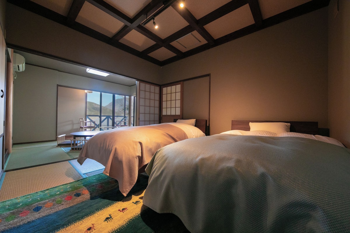 Een hotelkamer met twee bedden, tatami matten, een schuifdeur naar een balkon en een traditionele Japanse glijdeur.