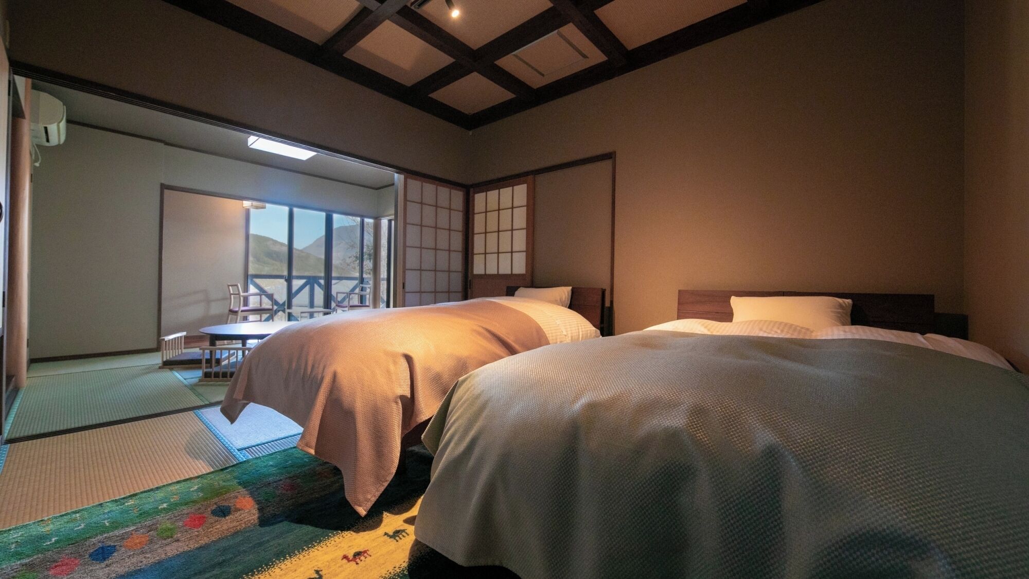Een traditionele Japanse kamer met tatami vloeren, twee bedden, een schuifdeur en uitzicht op een berg.