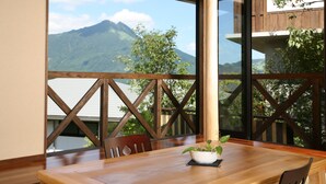 Una mesa de madera con sillas, una planta en maceta y vistas de una montaña a través de amplios ventanales.