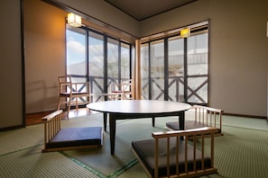 A traditional tatami room with a low table and benches, large windows, and a view of the outdoors.