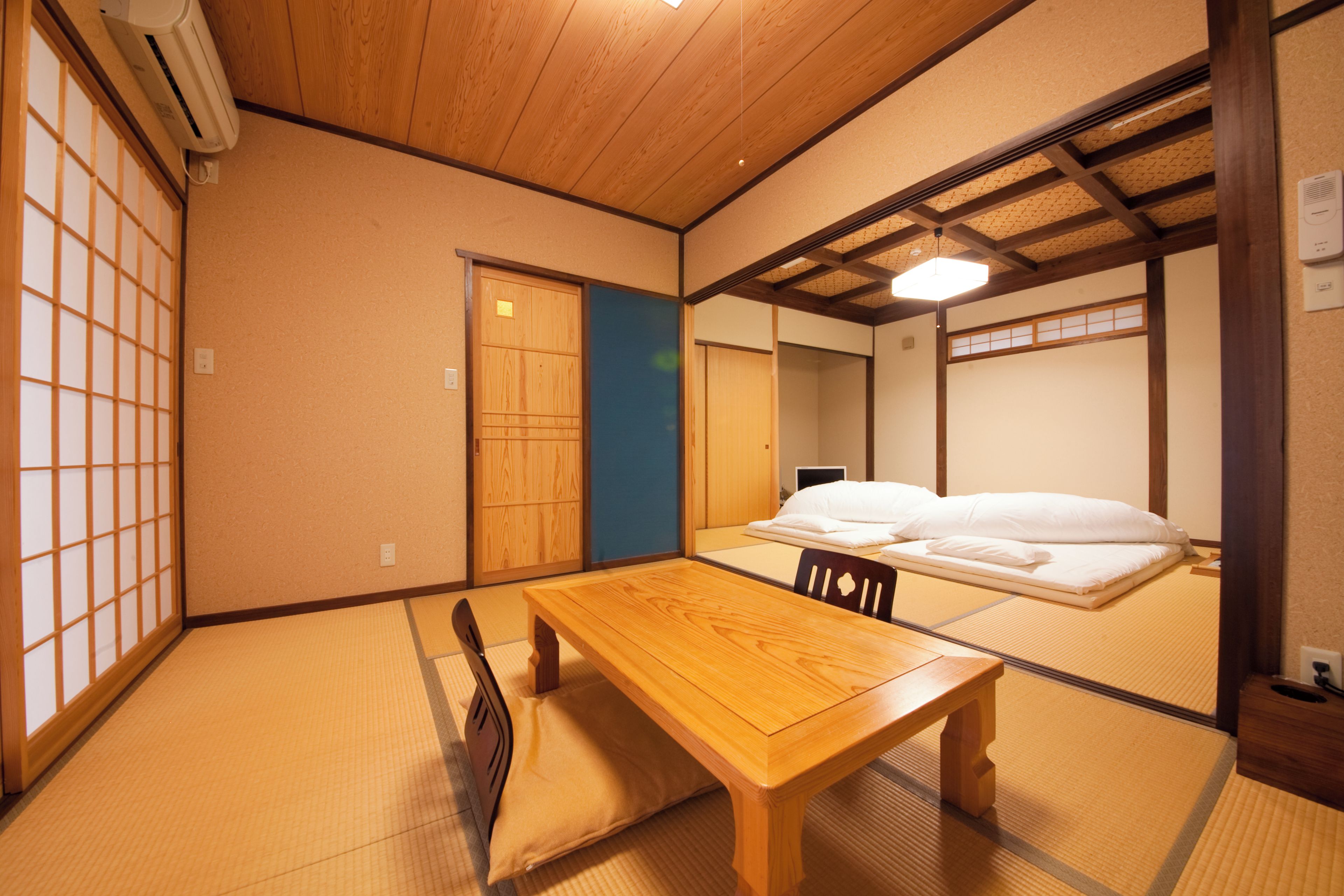 A traditional Japanese room with tatami flooring, a wooden table, a futon bed, and sliding doors.