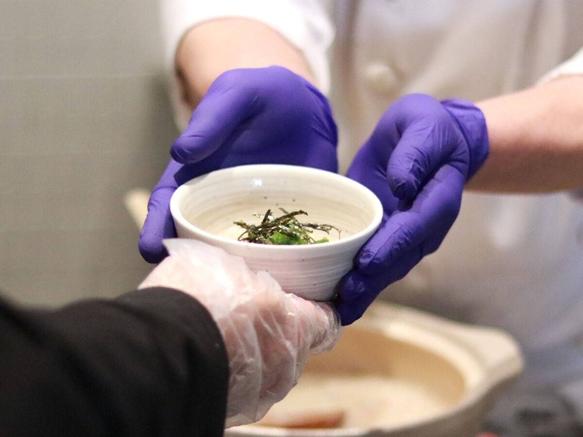 A person wearing gloves handling a bowl with seaweed.