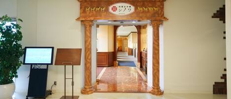 A hotel entrance with a wooden archway, a reception desk, and a digital screen.