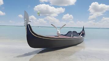 Un bote tradicional con una gaviota en la proa, anclado en una playa despejada con aguas tranquilas y una costa distante.