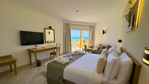 A hotel room with a bed, a desk, a TV, and a balcony with a view of the sea.